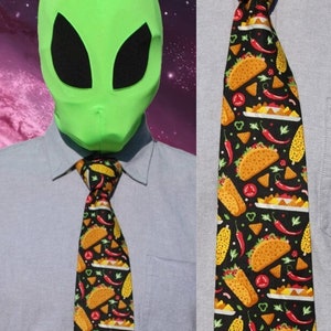 May include: A black tie with a repeating pattern of tacos, chili peppers, corn, and nachos. The tie is worn with a light blue collared shirt. The tie's design features yellow, red, and green elements.