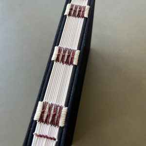 May include: A black fabric-covered book with white and maroon stitching along the spine.