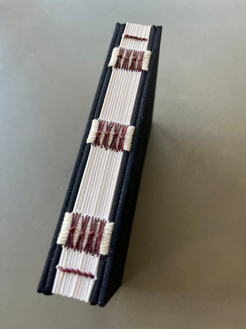 May include: A black fabric-covered book with white and maroon stitching along the spine.