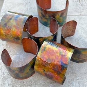 May include: Five copper bracelets with a hammered texture and iridescent patina in shades of green, blue, orange, and red.