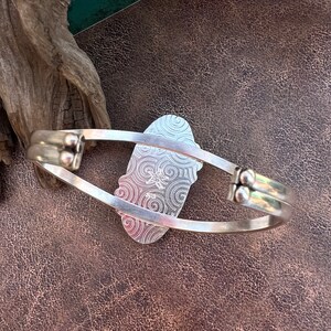 K&ouml;nnte beinhalten: Silberarmband mit einem dekorativen, wirbelnden Muster auf der R&uuml;ckseite. Das Armband ist offen und hat einen Scharnierverschluss.