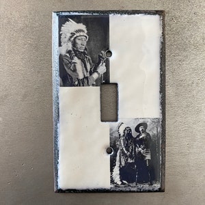 Puede incluir: Una placa de interruptor de luz de cerámica blanca con dos fotos en blanco y negro de hombres nativos americanos con tocados tradicionales. La foto superior muestra a un solo hombre, mientras que la foto inferior muestra a dos hombres de pie juntos.
