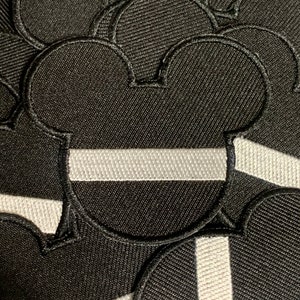 May include: A set of black felt patches shaped like Mickey Mouse ears with a white stripe across the middle.