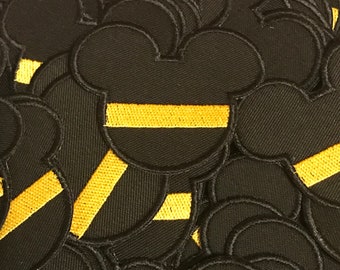 May include: A pile of black felt patches with a yellow stripe across the middle. The patches are shaped like a cartoon mouse head.