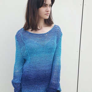 May include: A blue and turquoise knitted jumper with a loose fit and long sleeves. The jumper is made of a lightweight, open-weave fabric.