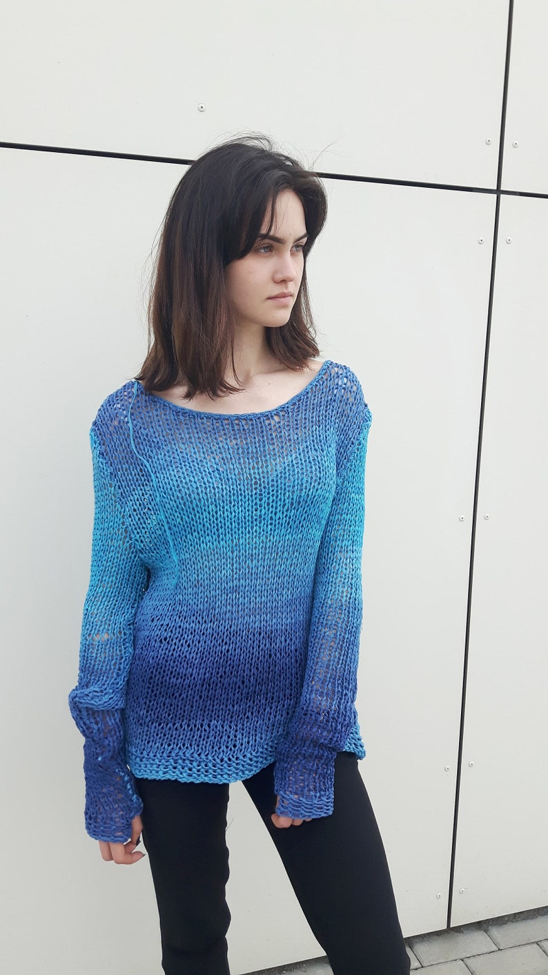 May include: A blue and turquoise knitted jumper with a loose fit and long sleeves. The jumper is made of a lightweight, open-weave fabric.