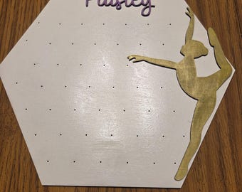 May include: White, hexagon-shaped jewelry organizer with the name "Paisley" in purple script. A gold-colored ballerina silhouette is on the right. The board has small holes for hanging jewelry.