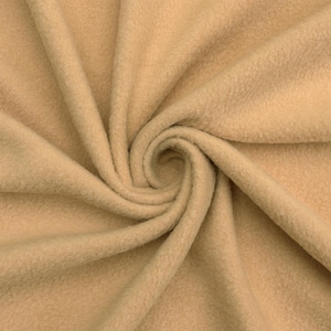 May include: A close-up of a soft, beige fleece fabric. The fabric is folded and draped, showing its texture and color.