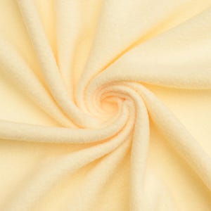 May include: A close-up of a soft, pale yellow fleece fabric. The fabric is folded and twisted, showing its texture and drape.
