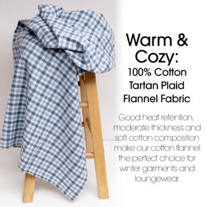 May include: A blue and white tartan plaid flannel fabric draped over a wooden stool. The fabric is 100% cotton and has a classic check pattern. Text on the right reads "Warm & Cozy: 100% Cotton Tartan Plaid Flannel Fabric."