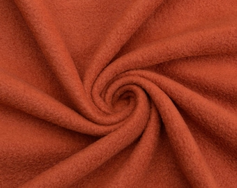 May include: Close-up of a rust-colored fleece fabric with a soft, fuzzy texture. The fabric is folded and draped, showing its drape and texture.
