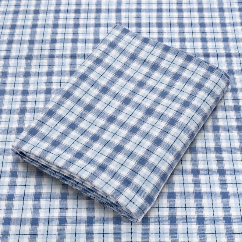 May include: Folded blue and white checkered fabric. The fabric has a classic plaid pattern with varying shades of blue and white, creating a visually appealing design. The fabric is neatly folded, showcasing the pattern's repetition.