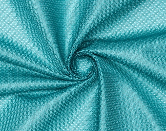 Op de afbeelding: Een close-up van een tealblauwe stof met een textuur, geweven patroon. De stof is gevouwen en gedraaid, waardoor een wervelend effect ontstaat.