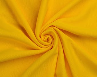 May include: A vibrant yellow fabric featuring a fine, textured mesh pattern. The material is gathered in a central spiral, creating deep, radiating folds and shadows that highlight the consistent color and the intricate, small-scale weave of the textile.