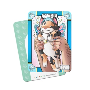 May include: A cartoon illustration of a calico cat wearing a crown and fairy wings. The cat is being held by two hands. The card has the text "FAERIE" and "1/1" on it.