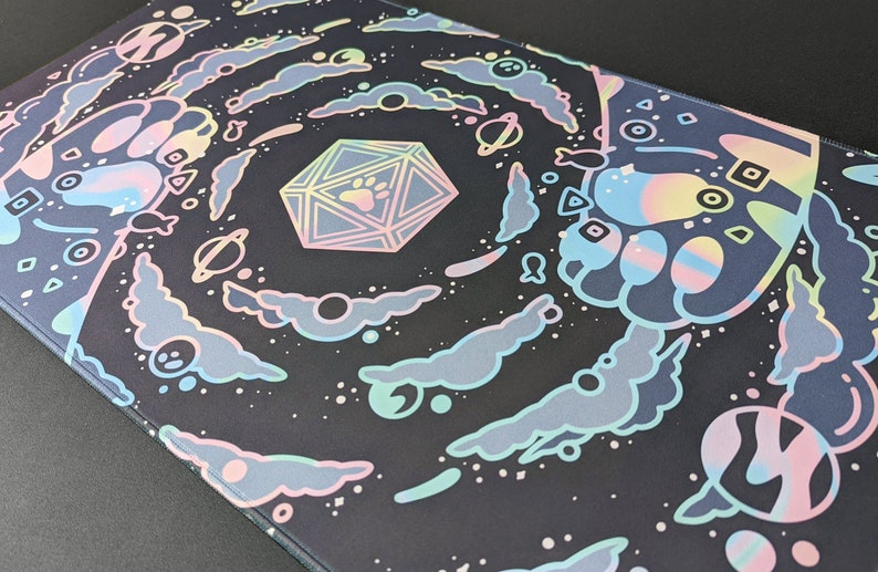Puede incluir: Un rat&oacute;n de ordenador negro y blanco con un dise&ntilde;o de galaxia en espiral. La galaxia est&aacute; llena de nubes, estrellas y planetas de color rosa pastel, azul y amarillo. Un dado grande, iridiscente, de m&uacute;ltiples caras con una huella de pata en cada lado est&aacute; en el centro del dise&ntilde;o.