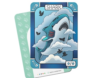 May include: A blue and white illustrated card with the word "SHARK" at the top. A cartoon shark with a toothy grin is flying through the clouds. The card has two stars at the bottom right corner.