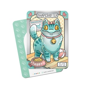 May include: A fantasy art card featuring a blue cat with yellow eyes, a pink bow, and a bell collar. The card is labeled "SHAPESHIFTER" and "TABBY". A second card with paw prints is visible.