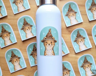 Könnte beinhalten: Eine weiße Wasserflasche mit einem Aufkleber eines Geparden, der einen braunen Zaubererhut auf einem blaugrünen Hintergrund trägt. Der Aufkleber ist von einem weißen Bogen umgeben. Die Flasche ist von mehreren Aufklebern mit dem gleichen Geparden umgeben, der einen Zaubererhut trägt.