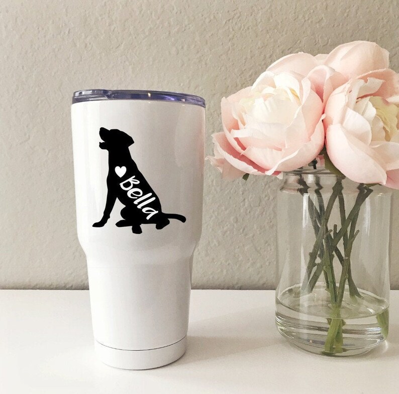 Puede incluir: Un vaso blanco de acero inoxidable con una silueta negra de un perro y el nombre "Bella" con un coraz&oacute;n.