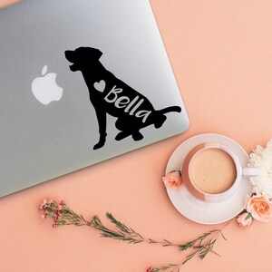 Puede incluir: Una silueta negra de un perro con un coraz&oacute;n y el nombre "Bella" en un lado. La pegatina est&aacute; en una computadora port&aacute;til plateada.