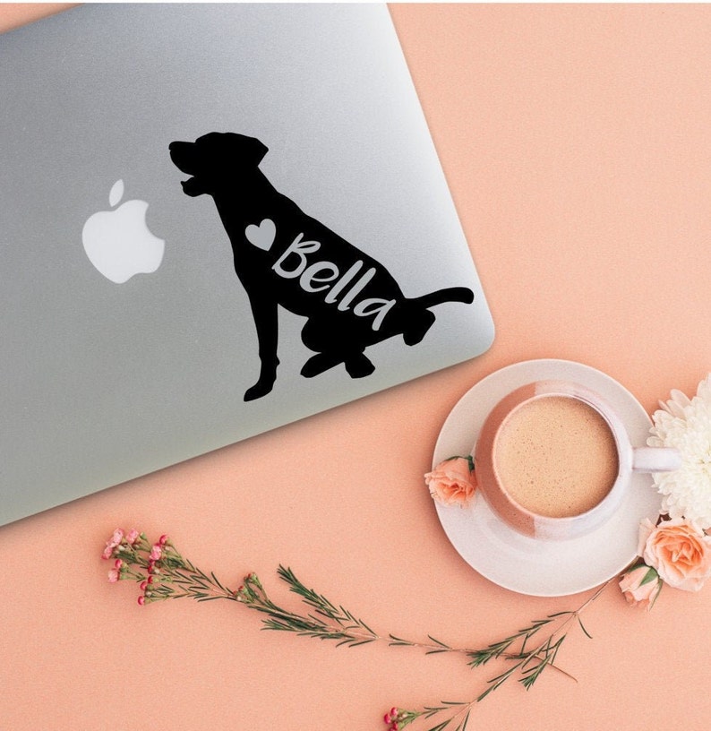 Puede incluir: Una silueta negra de un perro con un coraz&oacute;n y el nombre "Bella" en un lado. La pegatina est&aacute; en una computadora port&aacute;til plateada.