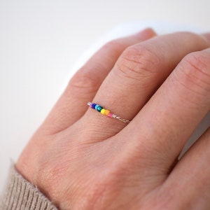 May include: A delicate rainbow beaded ring with a silver chain. The ring features small, colorful beads in a rainbow pattern.