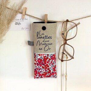 May include: A beige linen glasses case with a floral print lining. The case has a black button and the text "Les lunettes d'une Maitresse en Or" is embroidered on the front.