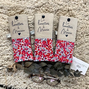 May include: Three red and white floral patterned eyeglass cases with the text "Les lunettes de Mamie" and "Les lunettes de Maminou" on the top flap. The cases are made of linen and have a button closure.