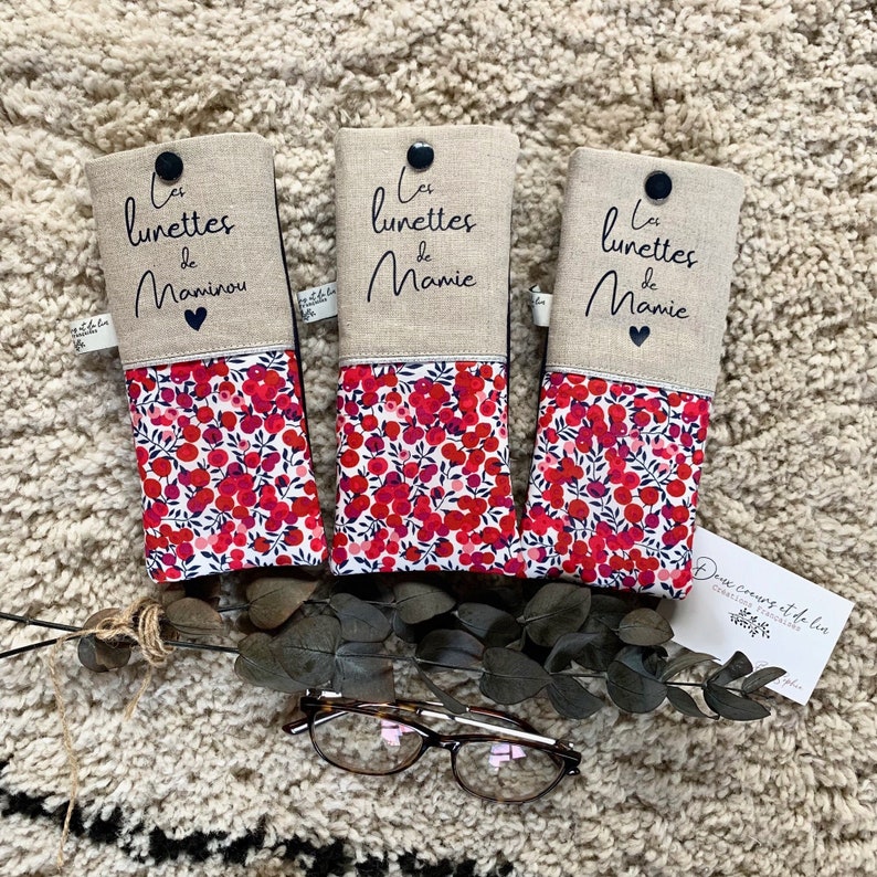 May include: Three red and white floral patterned eyeglass cases with the text "Les lunettes de Mamie" and "Les lunettes de Maminou" on the top flap. The cases are made of linen and have a button closure.