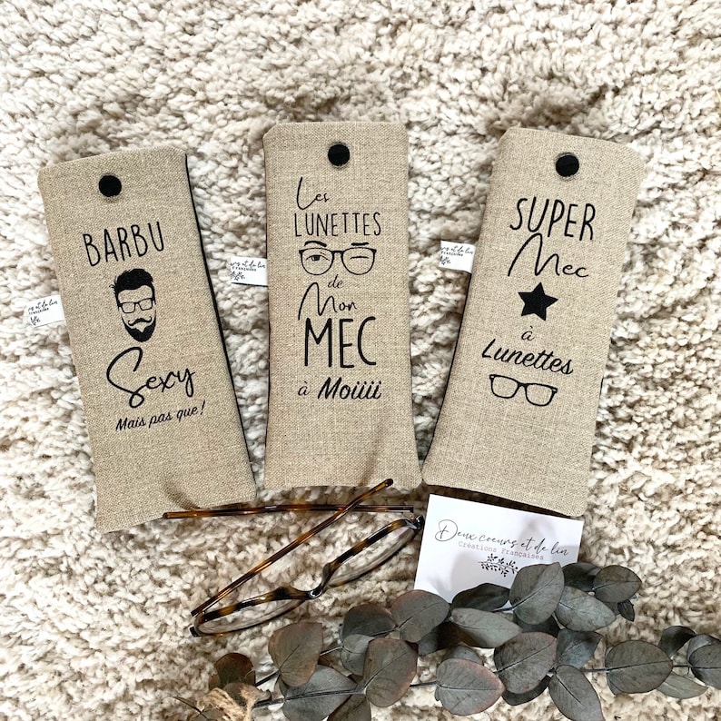 May include: Three beige linen eyeglass cases with black text and images. The cases feature the phrases "Barbu Sexy Mais pas que!" "Les Lunettes de Mon MEC &agrave; Mo&uuml;i" and "Super Mec &agrave; Lunettes".
