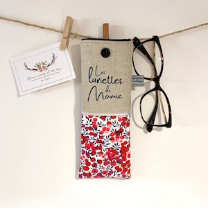 May include: A beige linen glasses case with a floral fabric lining. The case has a button closure and the text "Les lunettes de Mamie" is embroidered on the front.