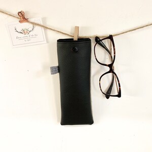 May include: Black leather glasses case hanging from a string with a pair of tortoiseshell glasses hanging below it.
