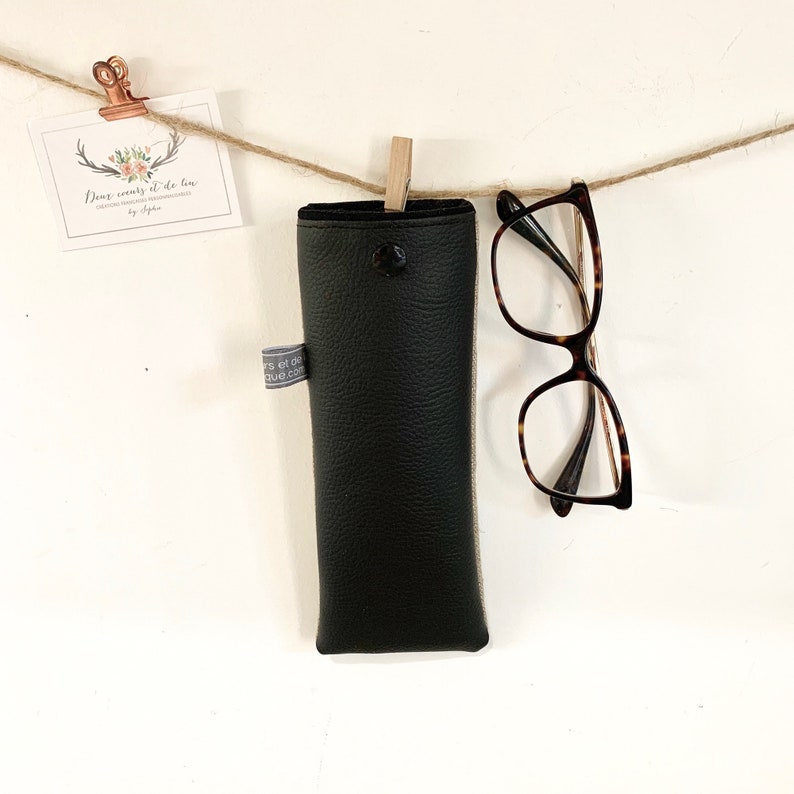 May include: Black leather glasses case hanging from a string with a pair of tortoiseshell glasses hanging below it.