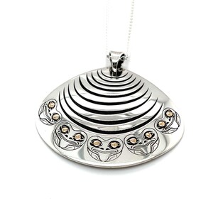 May include: A silver pendant necklace with a distinctive design. The pendant has a clam shell shape with black lines and gold-coloured accents. The necklace features a fine silver chain.