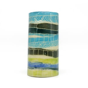 May include: A cylindrical ceramic vase with a blue, green and white striped pattern. The vase is decorated with a variety of geometric designs.