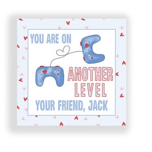 May include: A blue and white card with a light blue background and a white border. The card has a red heart pattern and two blue video game controllers. The text on the card reads "You are on another level. Your friend, Jack."