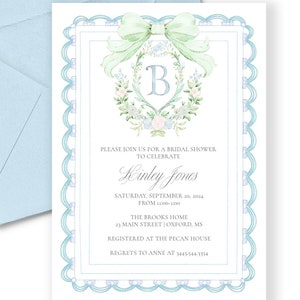 May include: A light blue envelope and a white invitation card with a scalloped border. The invitation features a floral wreath with a bow and the letter "B". Text on the card reads "Please join us for a bridal shower to celebrate Kinley Jones."