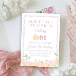 May include: A pink and white invitation card with the text "OUR LITTLE PUMPKIN is turning one". The card has a scalloped pink border and pumpkin illustrations. The invitation is for a first birthday celebration.