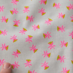 May include: Close-up of a white fabric with a repeating pattern of pink and yellow flowers. The flowers are stylized with a simple, geometric design. The fabric appears to be cotton or a similar lightweight material.
