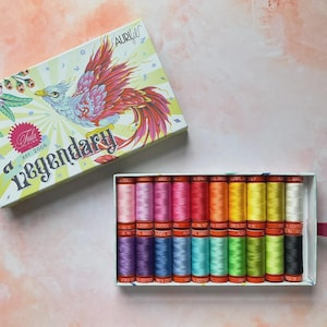 May include: A box set of Aurifil cotton thread spools in a variety of colors, with a decorative box featuring a phoenix illustration and the word "Legendary". The box is open, revealing the colorful thread spools.