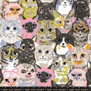 May include: A fabric print featuring a repeating pattern of various cat faces in diverse colors including pink, grey, yellow, and black. The cats have distinct facial markings and expressions. The bottom edge displays the text RUBY STAR SOCIETY.