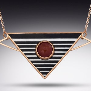 May include: A geometric pendant necklace featuring a triangular design with black and white stripes. A round, faceted, reddish-brown stone is set in the center. The necklace has a delicate gold-colored chain and frame.