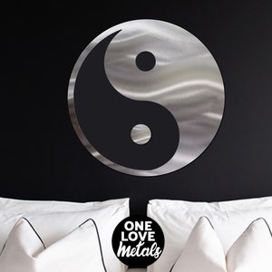 Peut inclure: Une d&eacute;coration murale en m&eacute;tal argent&eacute; repr&eacute;sentant le symbole yin yang avec une finition bross&eacute;e. Le symbole est suspendu &agrave; un mur noir au-dessus d'un lit blanc avec des oreillers blancs. Le texte "ONE LOVE metals" est visible en bas au centre de l'image.