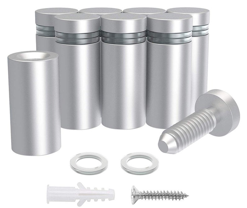 May include: A collection of silver-colored standoffs, designed for mounting. The set includes cylindrical standoffs, screws, washers, and wall anchors. The standoffs have a brushed metal finish and are designed to hold panels or signs.