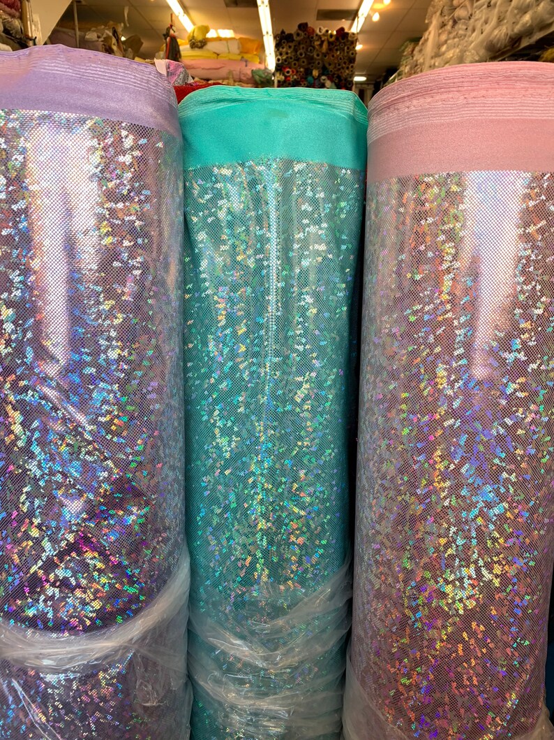 May include: Three rolls of iridescent fabric in purple, teal, and pink. The fabric has a glittery, holographic finish.