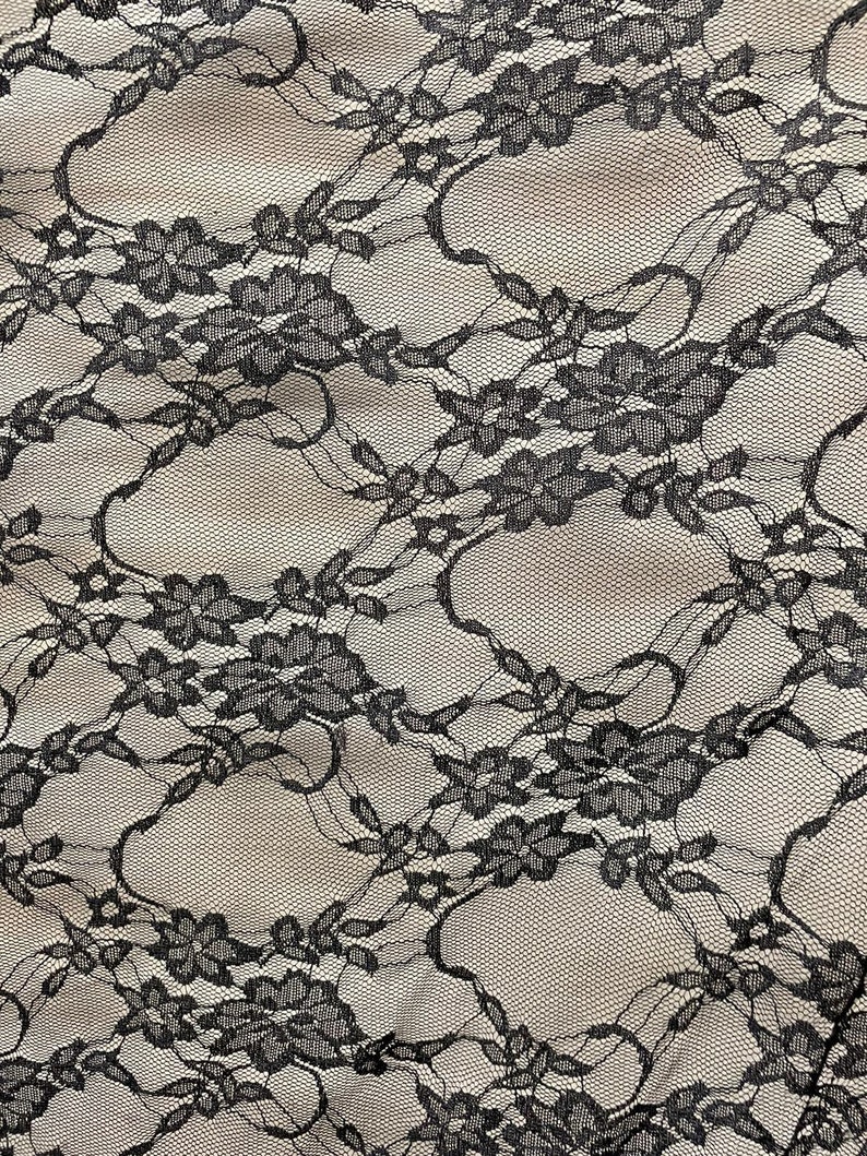 May include: Black lace fabric with a delicate floral pattern. The fabric is sheer and has a soft, flowing texture.