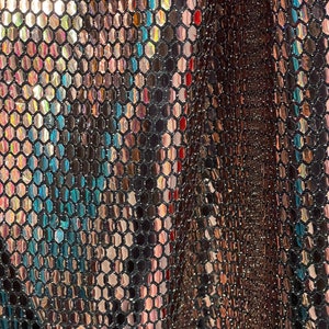 May include: Close-up of a metallic fabric with a hexagonal pattern. The fabric is iridescent, with shades of gold, silver, and bronze.