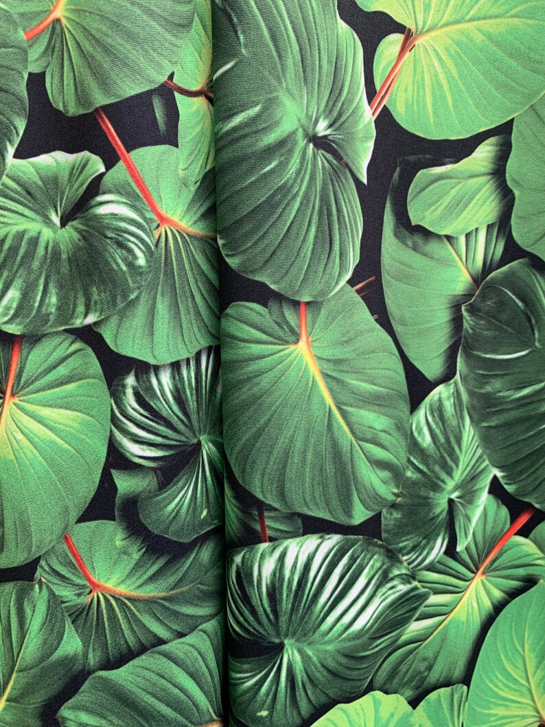 May include: A close-up of a fabric with a repeating pattern of large, green leaves on a black background.