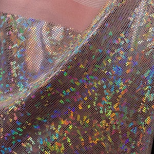 May include: A close-up of iridescent pink fabric with a textured, grid-like pattern. The fabric has a holographic finish that shimmers with rainbow colors.